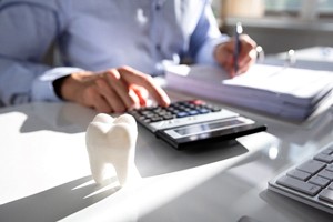 Man calculating cost of dental care with tooth nearby