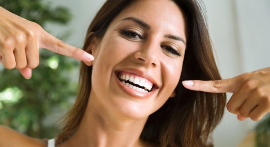 Woman with porcelain veneers pointing to her smile