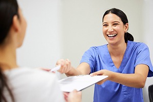 front desk staff member smiling and handing a form to a patient