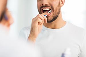 Man smiling while brushing his teeth