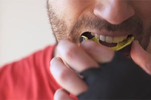 Man placing yellow and black mouthguard in mouth