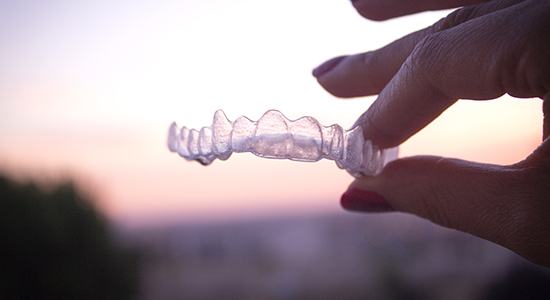 Hand holding an Invislaign clear aligner tray