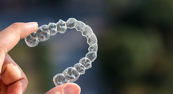 Hand holding Invisalign clear braces tray