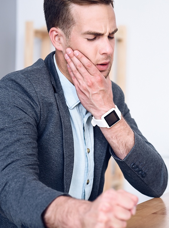 Man in need of T M J therapy holding jaw in pain