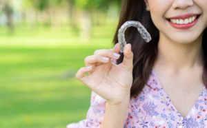 Woman stands outside in summer while holding Invisalign in Powell