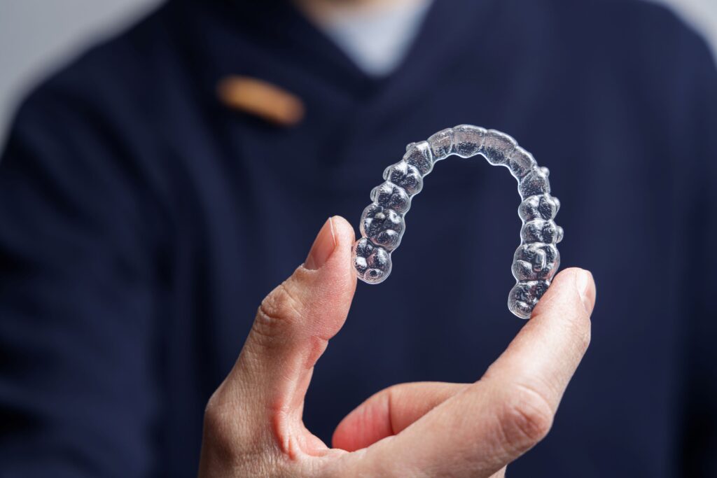 Dentist in blue scrubs holding a clear aligner