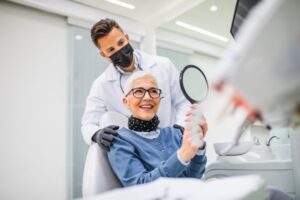 Patient smiling into mirror while dentist stands behind her.
